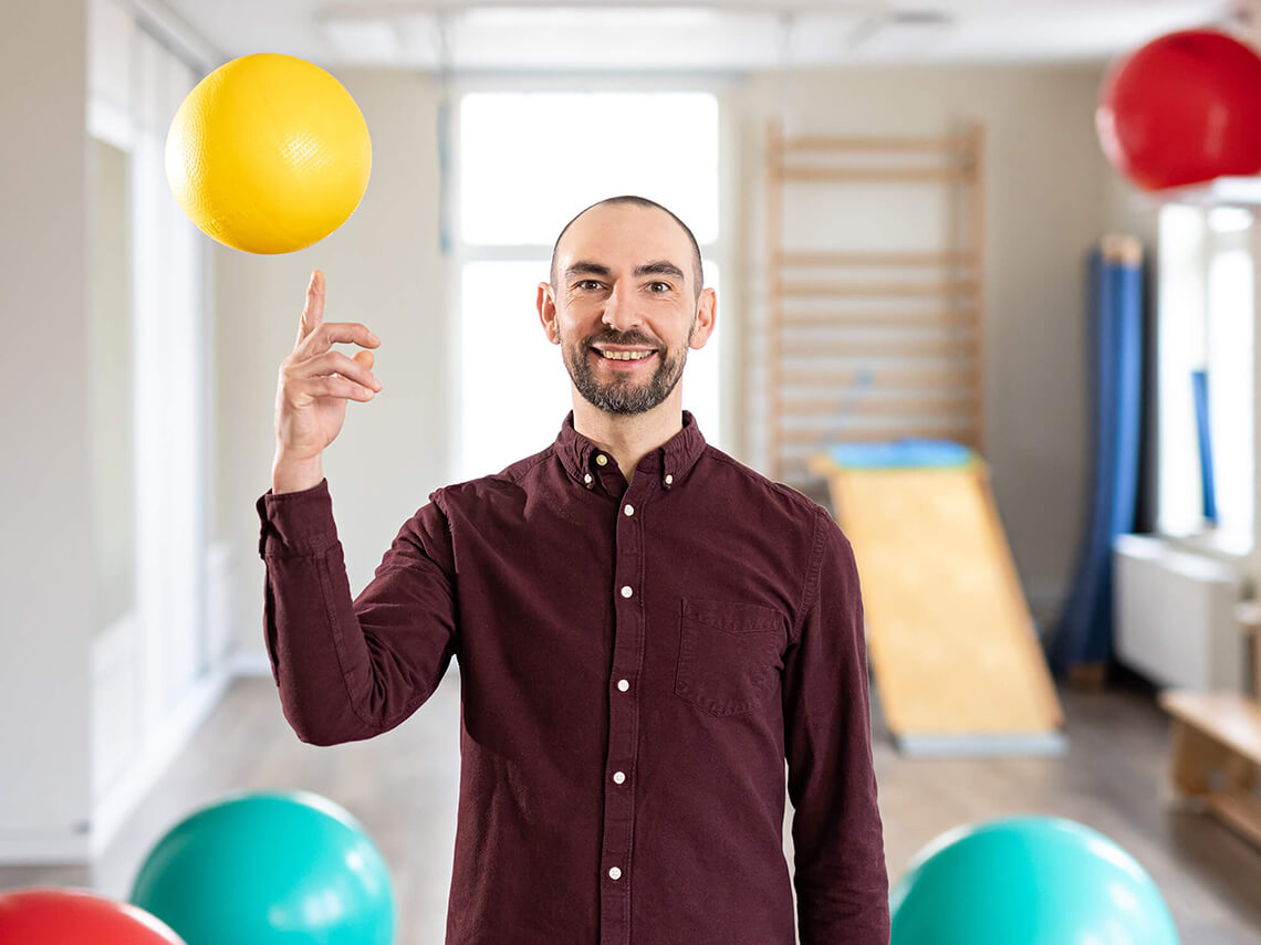 Robert Tippner balanciert gelben Ball auf dem Zeigefinger im Therapieraum.