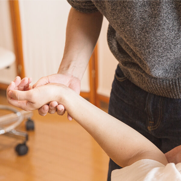 Therapeut mobilisiert das Handgelenk einer sitzenden Person