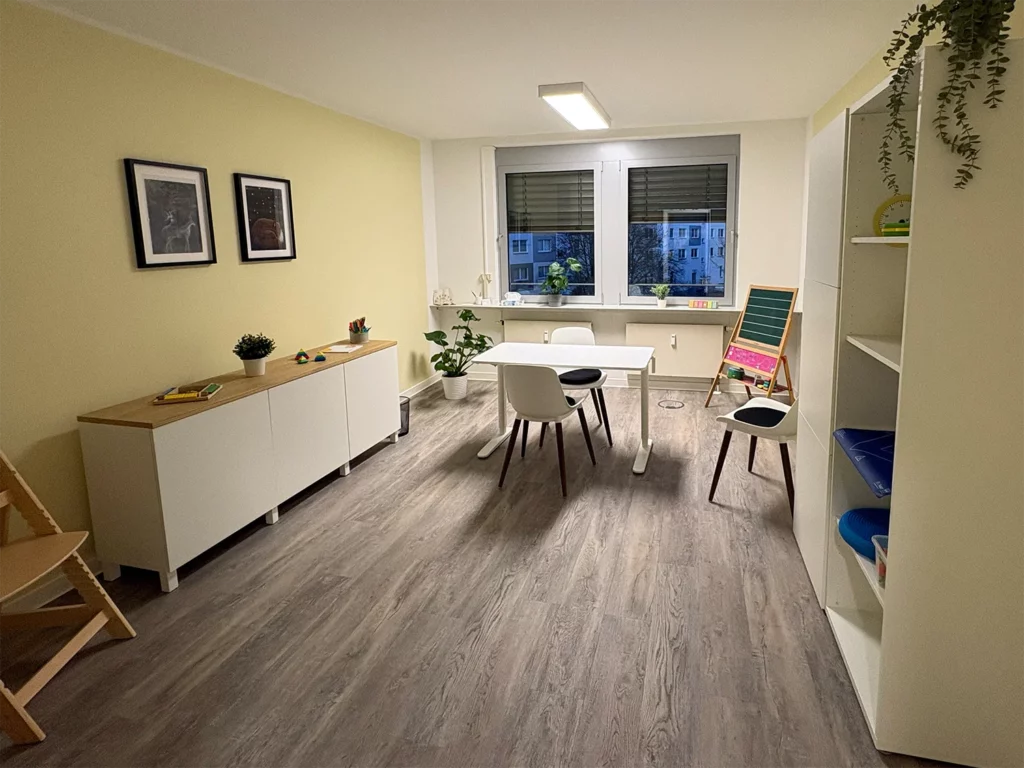 Therapieraum mit Tisch, Stühlen, Spiel- und Lernmaterialien sowie kindgerechter Einrichtung.