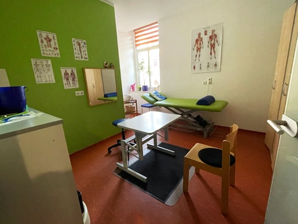 Behandlungsraum für Ergotherapie in Döbeln mit Therapieliege, Tisch und anatomischen Lehrtafeln